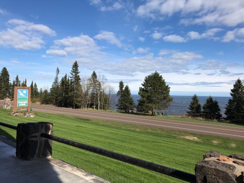 Scenic view of a lake with trees and a blue sky, featuring a sign for Cascade Lodge in the foreground.