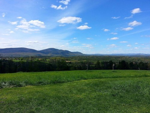 A scenic view of rolling green hills and mountains under a bright blue sky with fluffy white clouds.