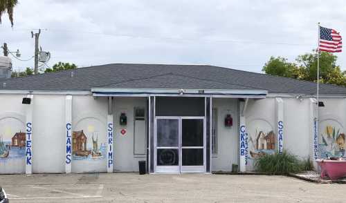 A restaurant exterior featuring murals of seafood and a flag, with a large glass entrance and a gray roof.