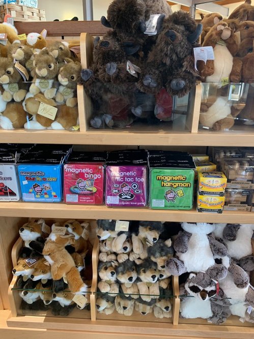 A display of plush toys and games, including magnetic bingo and tic-tac-toe, in a wooden shelf.