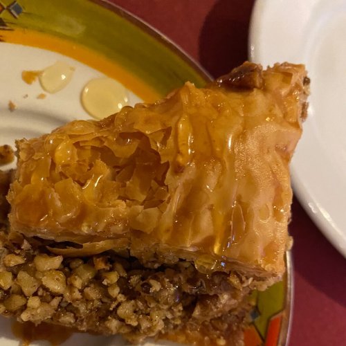 A slice of baklava drizzled with honey, resting on a colorful plate.