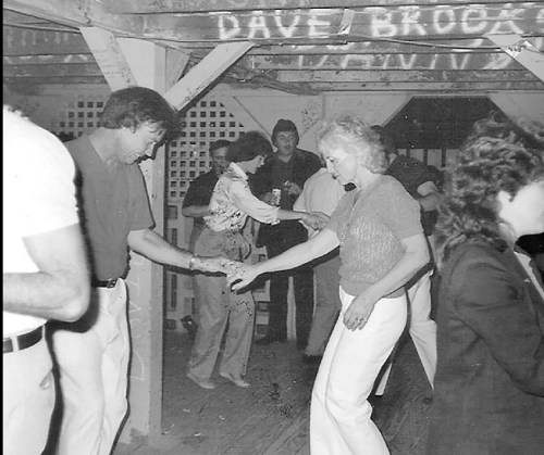 A black and white photo of people dancing indoors, with a lively atmosphere and vintage clothing styles.