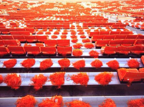 Empty stadium seats adorned with bright orange pom-poms, creating a vibrant and festive atmosphere.