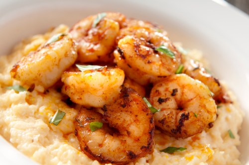 A bowl of creamy grits topped with seasoned, sautéed shrimp and garnished with fresh herbs.