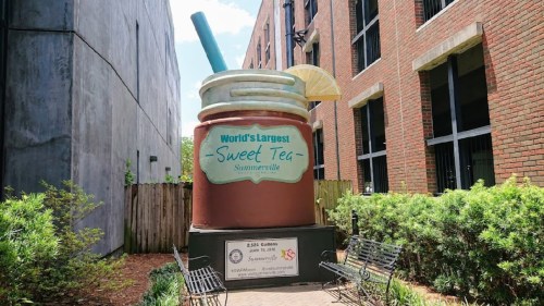A giant sweet tea cup sculpture in Summerville, featuring a straw and lemon slice, surrounded by greenery and benches.