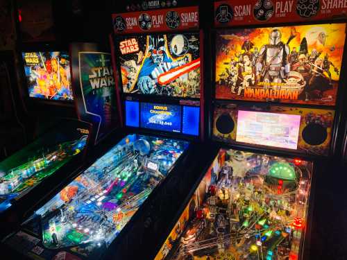 Three pinball machines featuring "Star Wars" and "The Mandalorian" themes, illuminated in a dimly lit arcade.