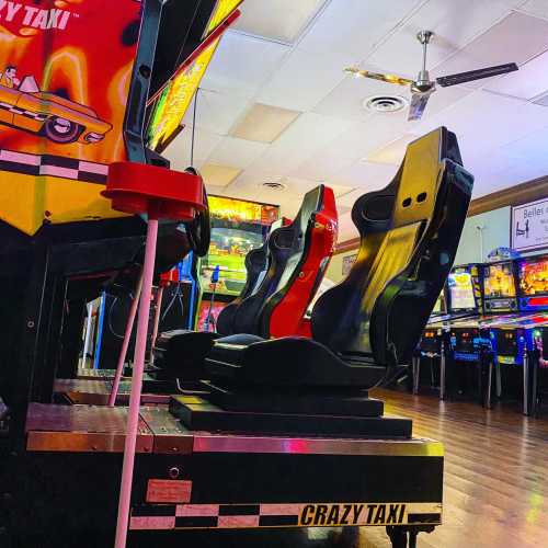 A colorful arcade with a "Crazy Taxi" game and two racing seats, illuminated by vibrant lights.