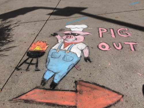 Chalk drawing of a pig in a chef's hat next to a grill, with the text "PIG OUT" and an arrow pointing right.