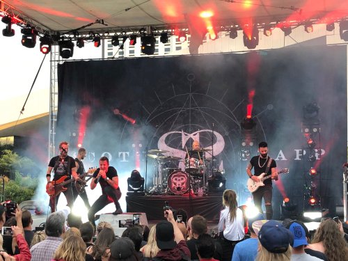 A rock band performs on stage with vibrant lights, while an enthusiastic crowd watches from below.