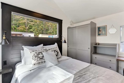 Cozy bedroom featuring a bed with decorative pillows, a gray wardrobe, and a desk by a large window.