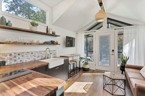 Bright, modern kitchen with wooden countertops, open shelving, and large windows overlooking a garden. Cozy seating area included.
