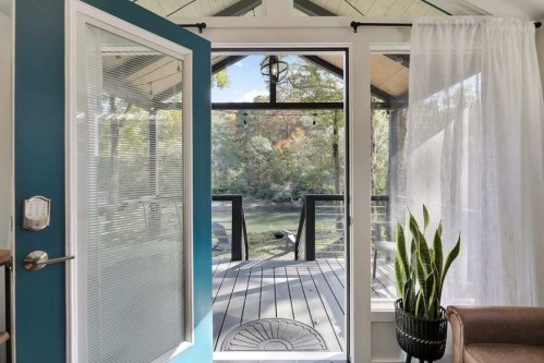 A view through a glass door showcasing a deck overlooking a serene, wooded area with a plant in the foreground.