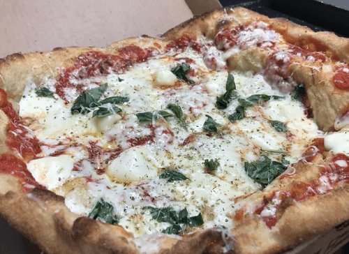 A close-up of a cheesy pizza with tomato sauce and fresh basil, served in a pizza box.