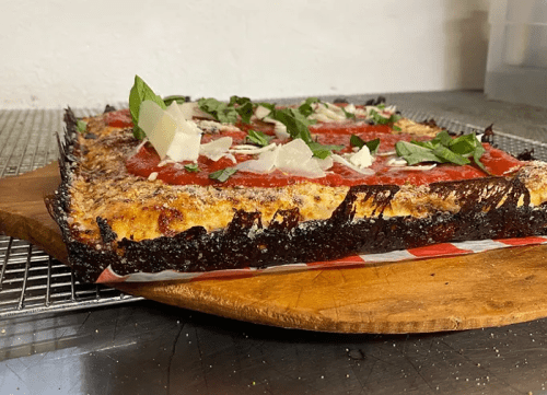 A rectangular pizza with a crispy crust, topped with tomato sauce, cheese, and fresh basil, on a wooden board.