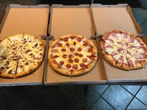 Three pizzas in open boxes: one with white cheese, one with pepperoni, and one with ham and pineapple.