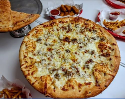 A large cheese pizza with toppings, surrounded by fries and chicken bites on a table.