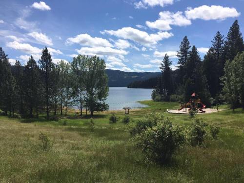 A serene lakeside scene with trees, a grassy area, and a playground in the foreground under a blue sky with clouds.