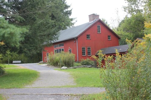 A red barn-style building surrounded by greenery and a gravel path, set in a peaceful outdoor environment.