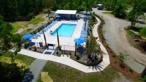 Aerial view of a swimming pool surrounded by lounge chairs and umbrellas, with landscaped areas nearby.