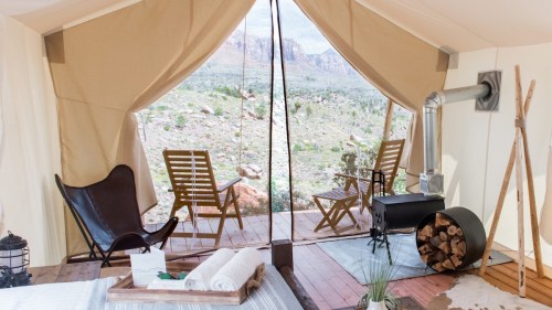 Cozy glamping tent interior with a view of mountains, featuring a wood stove, chairs, and a rustic decor.