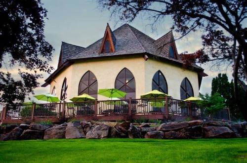 A unique, round building with a peaked roof, surrounded by green grass and patio umbrellas on a wooden deck.