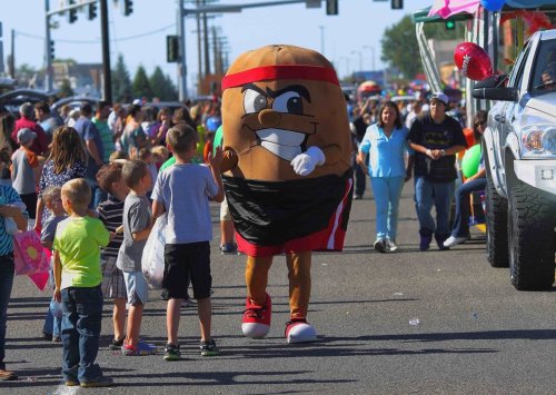 A large mascot in a brown costume with a smiling face walks among children at a lively street parade.