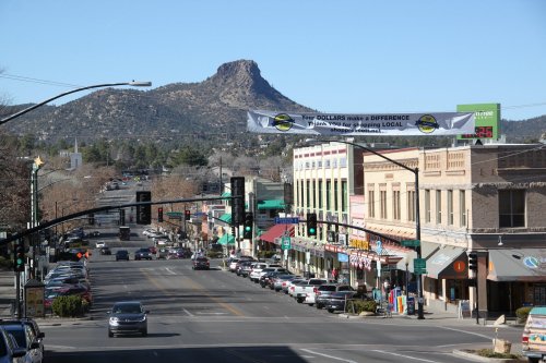 A view of a downtown street with shops, cars, and a mountain in the background under a banner promoting local spending.