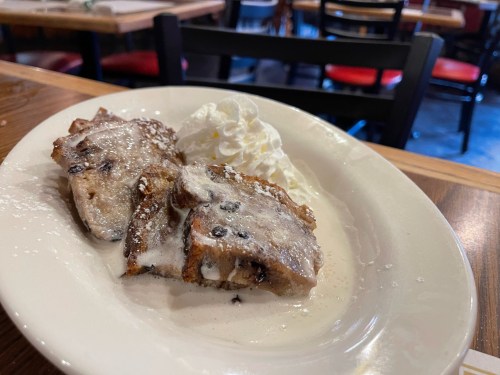 A plate of French toast topped with whipped cream and powdered sugar, served in a cozy restaurant setting.