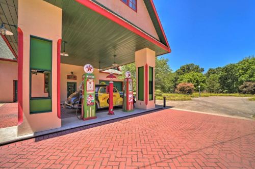 An old-fashioned gas station with vintage pumps and a classic car parked under a colorful canopy on a sunny day.