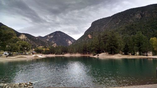 A serene lake surrounded by mountains and trees under a cloudy sky.