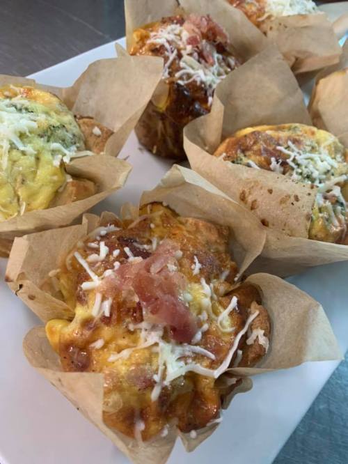 Baked savory muffins topped with cheese and bits of bacon, served in paper liners on a white plate.