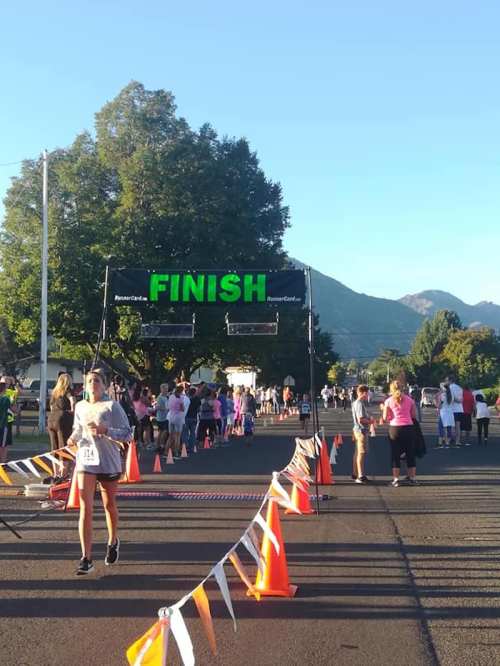 A runner approaches the finish line marked by a large green "FINISH" sign, with spectators and trees in the background.
