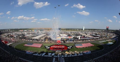 Aerial view of Charlotte Motor Speedway during a race, featuring fireworks, flags, and a crowd in attendance.