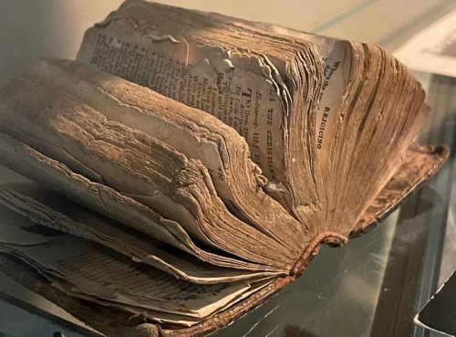 An old, worn book with frayed pages displayed in a glass case, showcasing its aged condition.