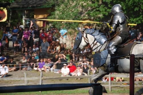 A knight in armor on horseback prepares to joust in front of a large crowd at a medieval event.