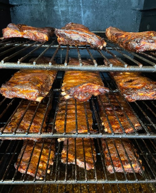 Close-up of a smoker filled with racks of juicy, smoked ribs, showcasing a rich, caramelized glaze.