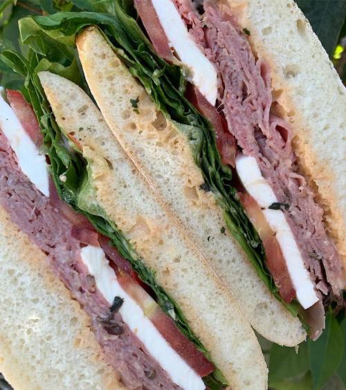 A close-up of a layered sandwich with lettuce, tomato, ham, and cheese on soft bread, cut into quarters.