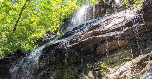 A serene waterfall cascading down a rocky cliff, surrounded by lush green trees and sunlight filtering through the leaves.