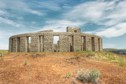 A stone structure resembling Stonehenge, set against a blue sky and grassy landscape.