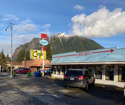 A cafe with a sign reading "Tweeter's Cafe" in front of a mountain, with cars parked nearby and a clear blue sky.