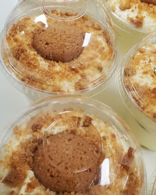 Close-up of dessert cups with layers of cream, crumbled cookies, and a whole cookie on top.
