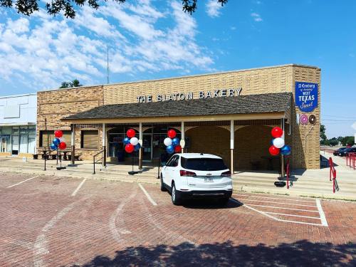Exterior of Slaton Bakery with red, white, and blue balloons, a parked white car, and a clear blue sky.