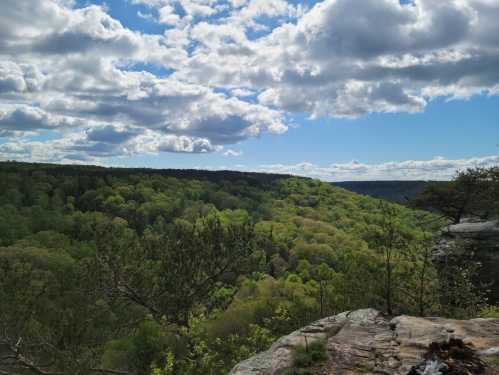 A scenic view of lush green hills under a partly cloudy sky, with rocky outcrops in the foreground.