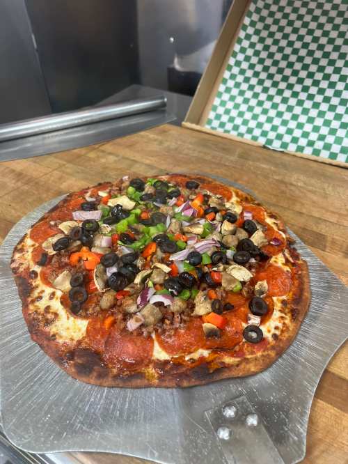 A freshly baked pizza topped with pepperoni, olives, green peppers, red onions, and sausage on a wooden surface.