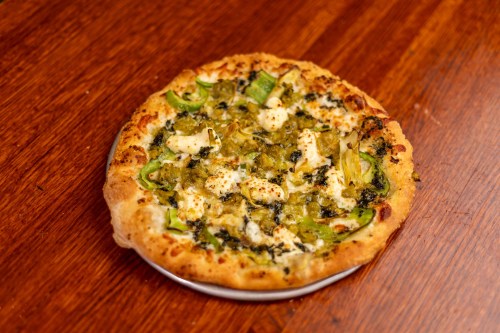 A freshly baked pizza topped with green peppers, chicken, and herbs on a wooden table.