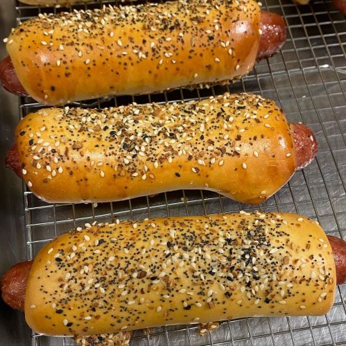 Three sesame-seeded hot dogs wrapped in golden-brown dough, resting on a cooling rack.