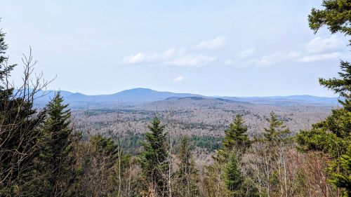 A panoramic view of rolling mountains and dense forests under a clear sky.
