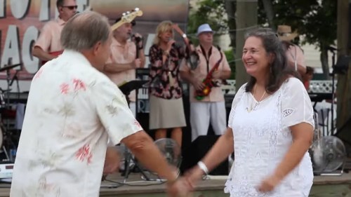 A couple dances joyfully in front of a live band, enjoying a lively outdoor music event.