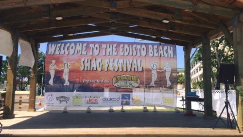 Banner for the Edisto Beach Shag Festival, featuring colorful text and a festive design, displayed on a wooden stage.