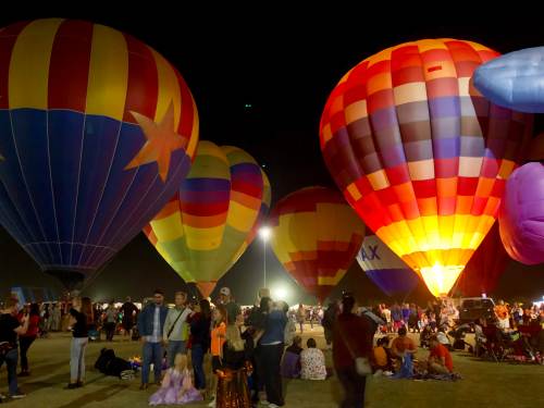 Colorful hot air balloons illuminated at night, surrounded by a crowd enjoying a festive atmosphere.